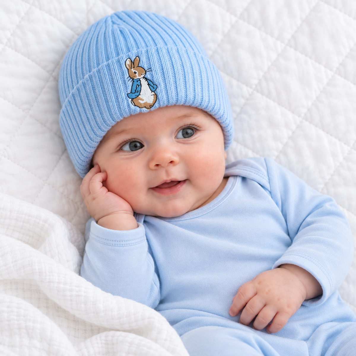 Baby wearing a blue ribbed knitted hat with an embroidered brown bunny in a blue jacket on the folded cuff.