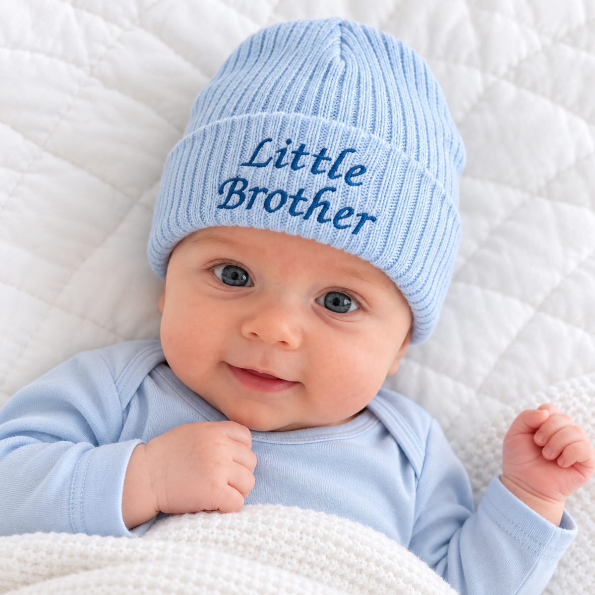 Baby boy wearing a pale blue ribbed knitted hat with dark blue Little Brother embroidery on the folded cuff.