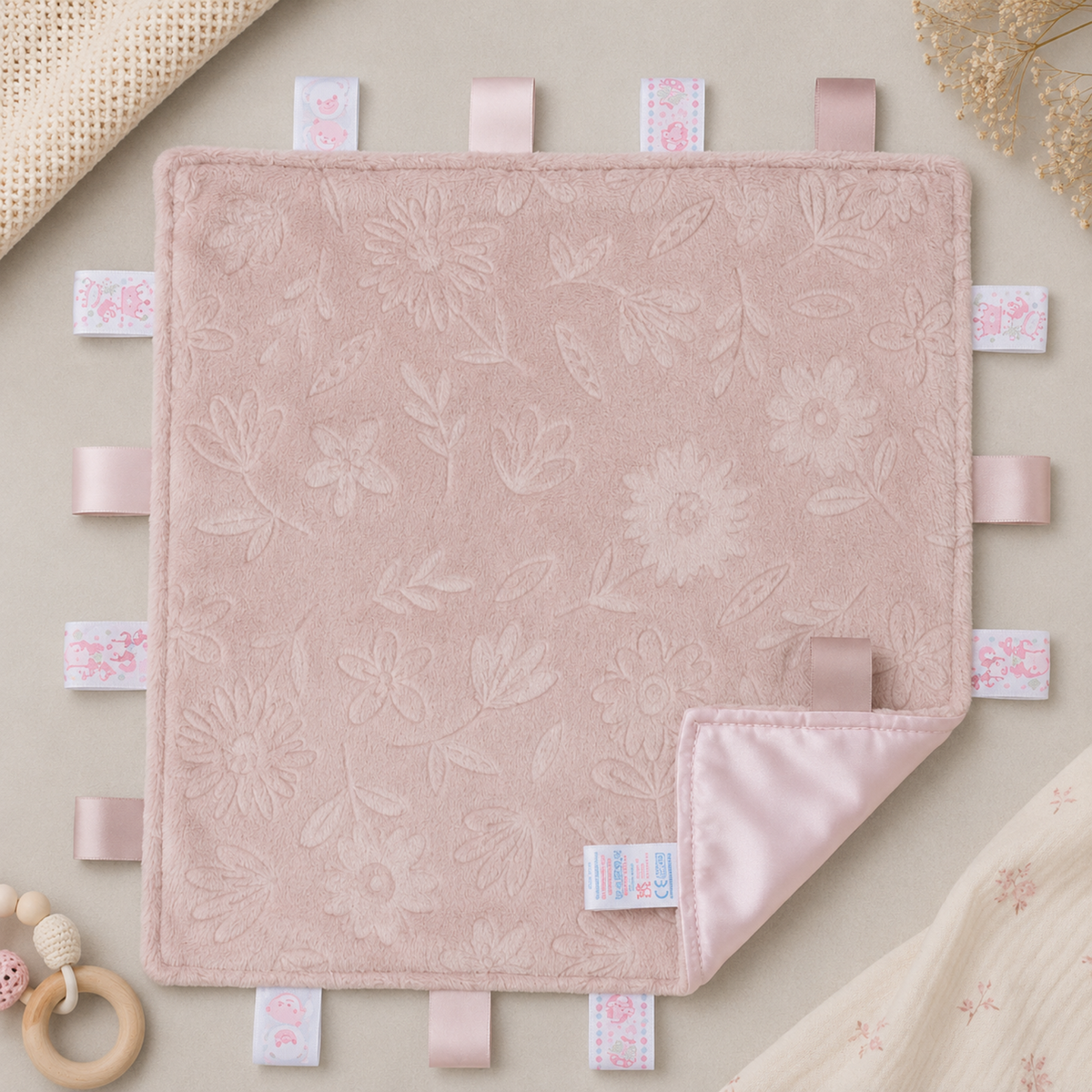 Embossed dusty pink floral baby taggy blanket with sensory ribbon tags and matching silky reverse measuring 35 x 35cm.