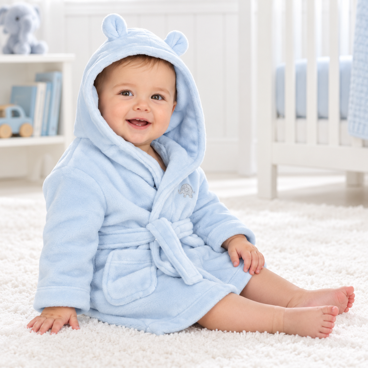 Happy baby wearing a pale blue hooded bathrobe with bear ears and embroidered elephant