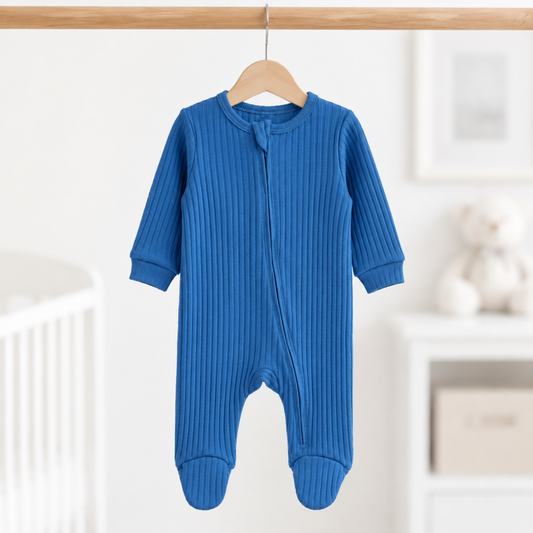 Azure blue ribbed cotton baby boy sleepsuit with long sleeves, front zip fastening and enclosed feet, size 0–3 months, hanging in a nursery.
