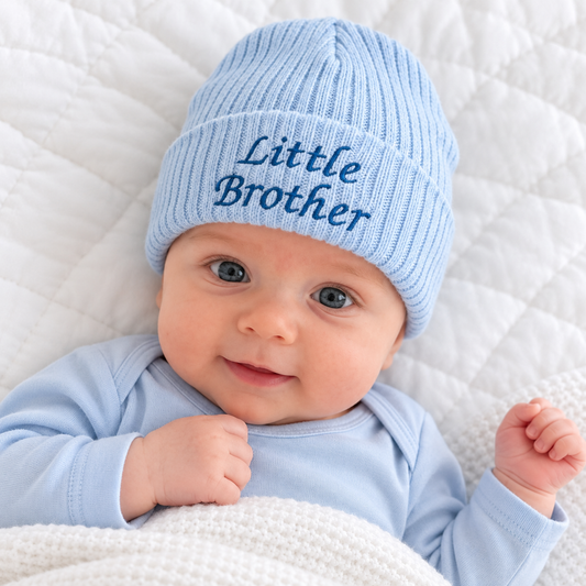 Baby boy wearing a pale blue ribbed knitted hat with dark blue Little Brother embroidery on the folded cuff.