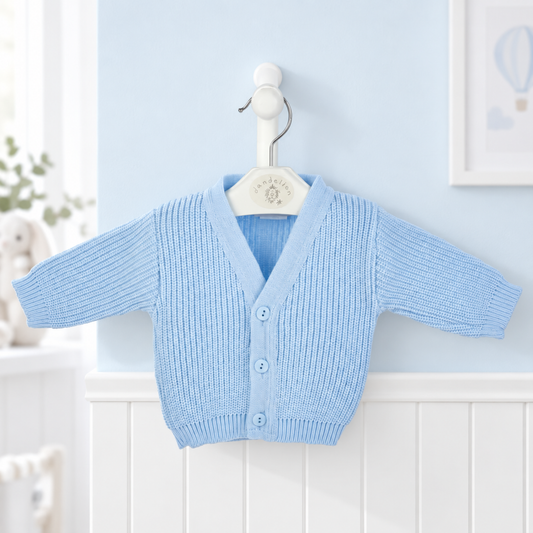 A light blue ribbed knit baby cardigan sweater with long sleeves and three front buttons, hanging on a white hanger against a pale blue wall and white wainscoting.