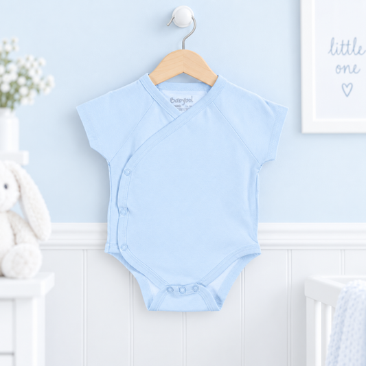 A light blue baby wrap bodysuit hanging on a wooden hanger against a pale blue wall, with a bunny plush and nursery decor visible in the background.