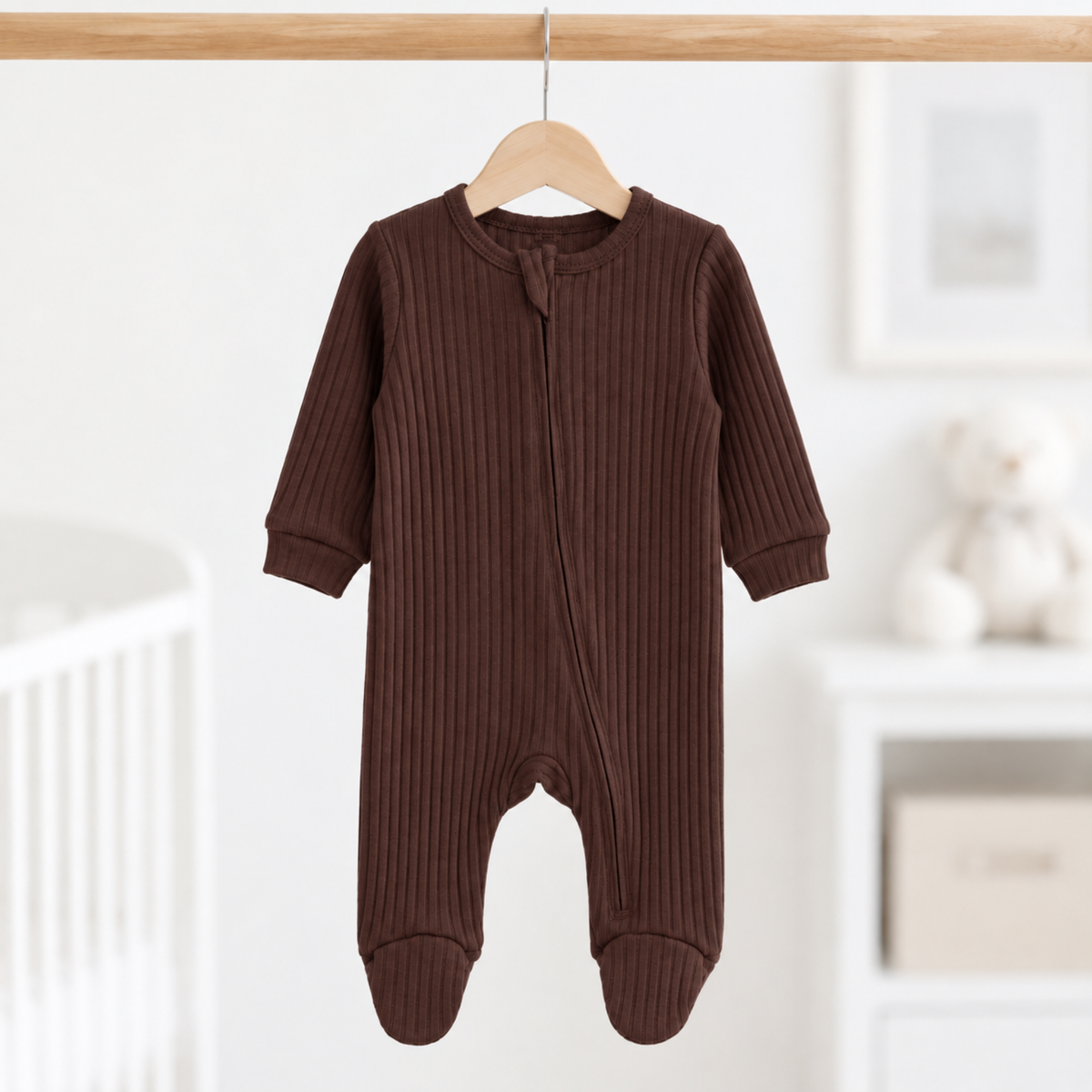 Chocolate brown ribbed cotton baby sleepsuit with long sleeves, enclosed feet and front zip fastening, size 0–3 months, hanging in a neutral nursery