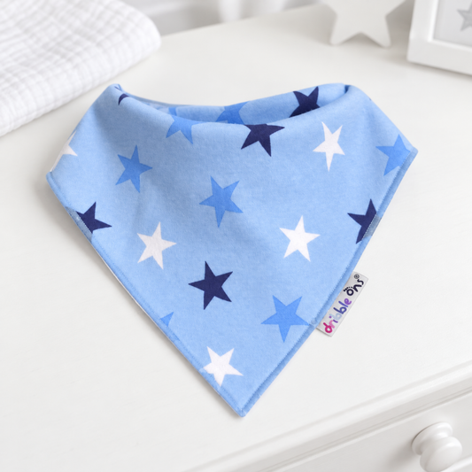 A light blue baby bandana bib with a star pattern in navy, medium blue, and white, resting on a white wooden surface.