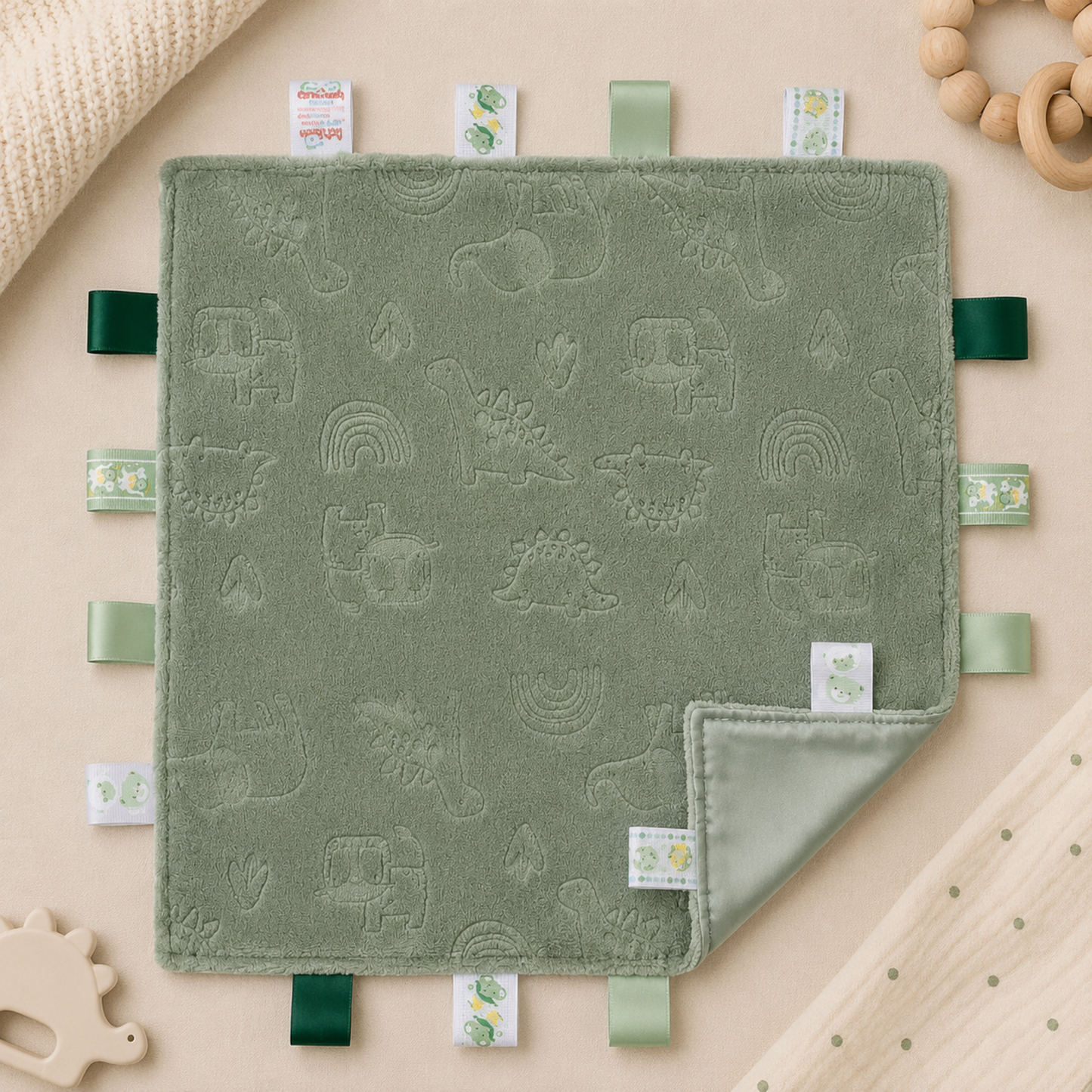 Embossed sage green dinosaur baby taggy blanket with sensory ribbon tags measuring 35 x 35cm.