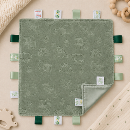Embossed sage green dinosaur baby taggy blanket with sensory ribbon tags measuring 35 x 35cm.