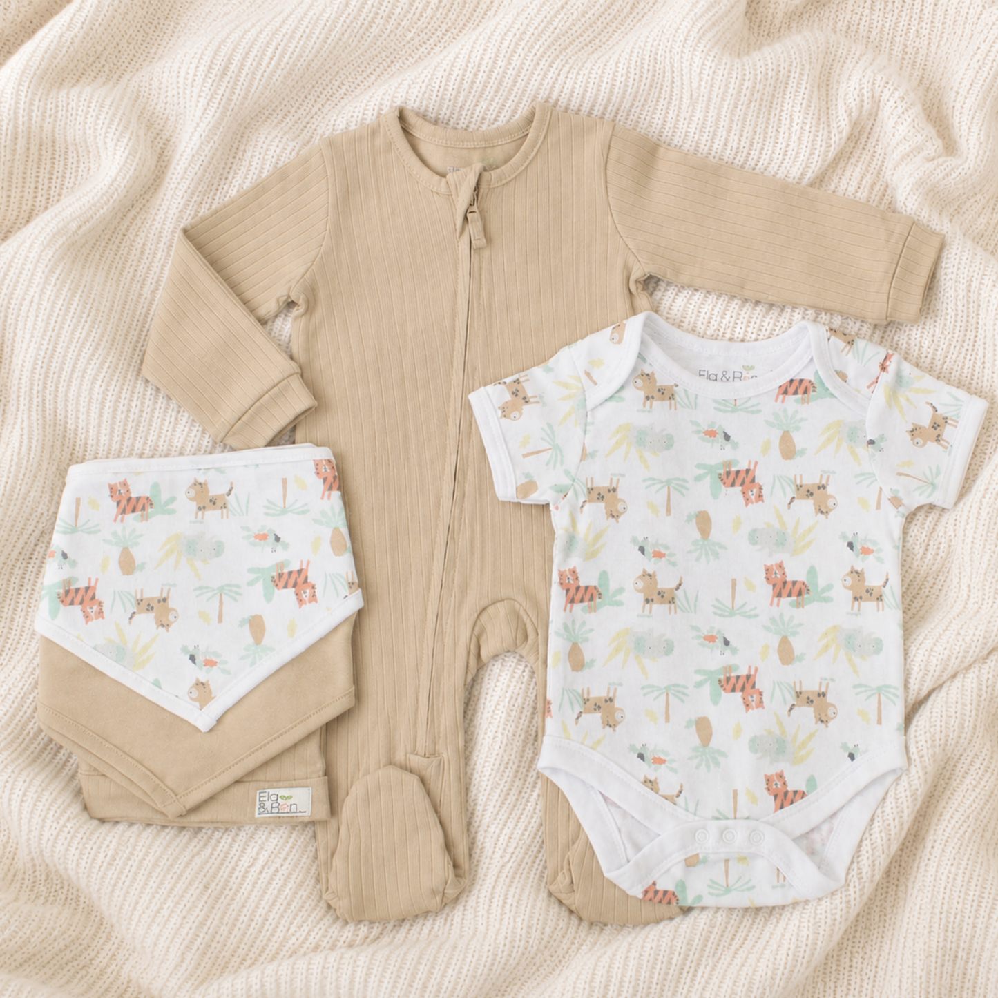 Baby clothing set with beige romper, bibs, hat and patterned onesie on a soft blanket
