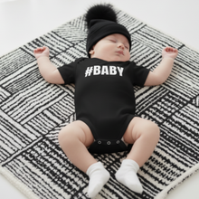 Load image into Gallery viewer, Baby wearing a black onesie with &#39;#BABY&#39; text 
