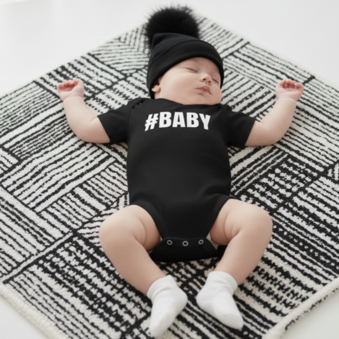 Baby wearing a black onesie with '#BABY' text 