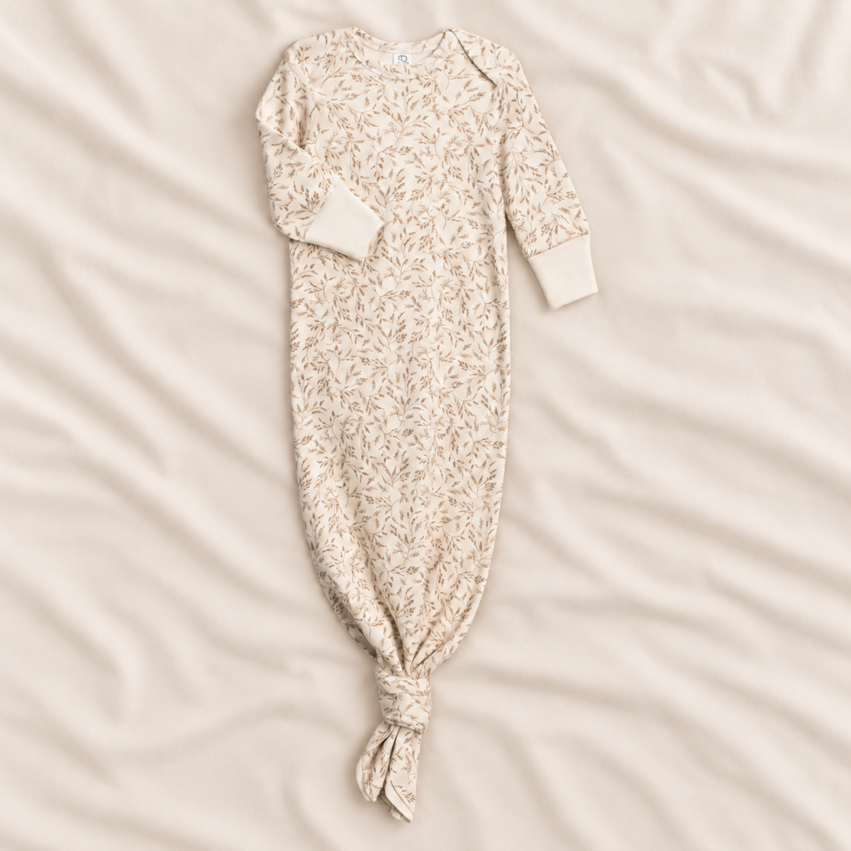 A long-sleeve baby sleep sack with an all-over delicate floral print, laid flat on a soft, cream-colored fabric background.