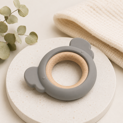 A gray silicone baby teether with a natural wood ring