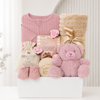Baby girl gift hamper with dusky pink sleepsuit, teddy bear, knitted booties, plush baby blanket, milestone discs and chocolate gift for new mum