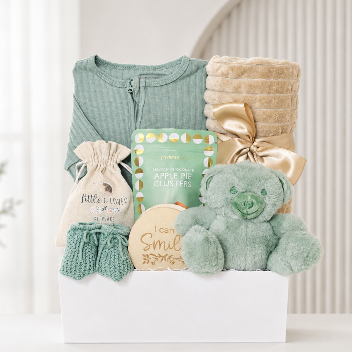 Unisex new baby gift hamper with sage green sleepsuit, teddy bear, knitted booties, beige baby blanket, milestone discs and chocolates for new mum