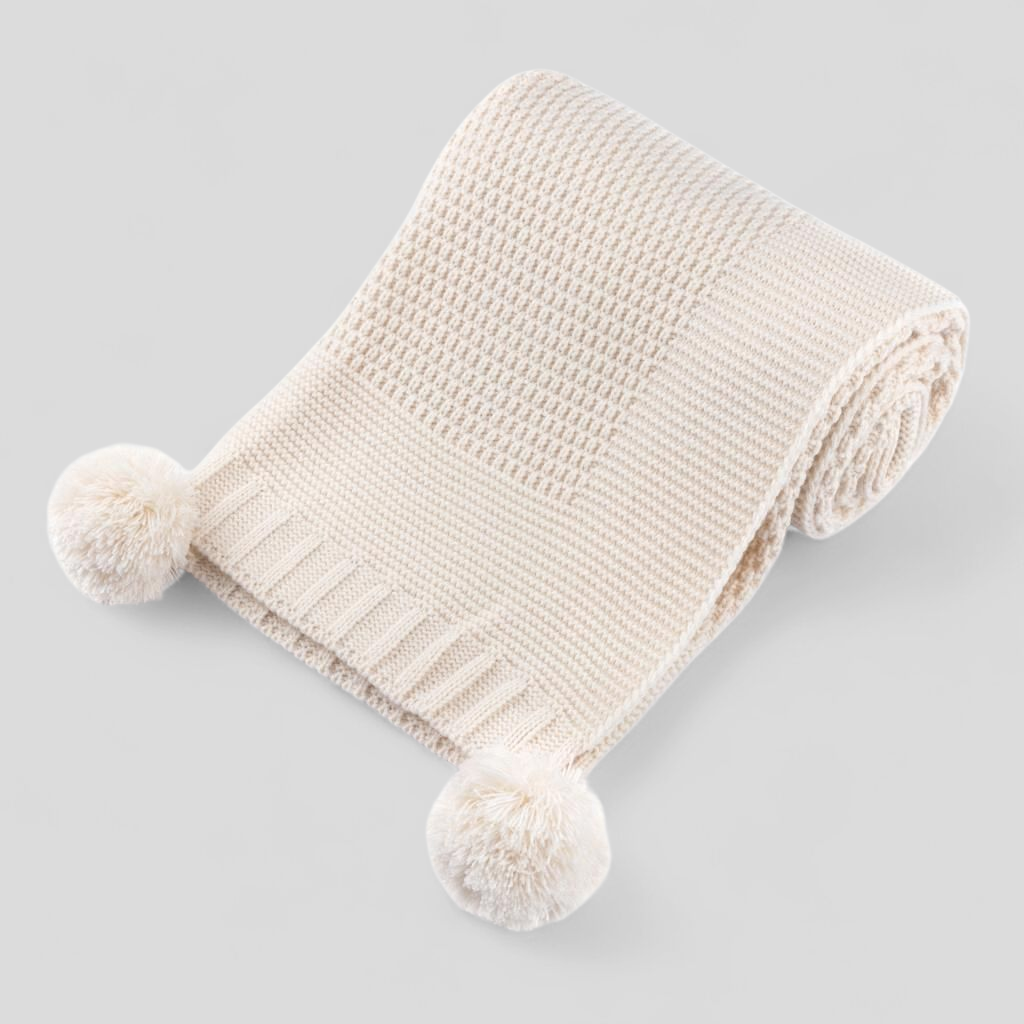 Beige knitted baby blanket with pom-poms