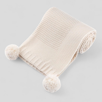 Beige knitted baby blanket with pom-poms