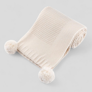 Beige knitted baby blanket with pom-poms