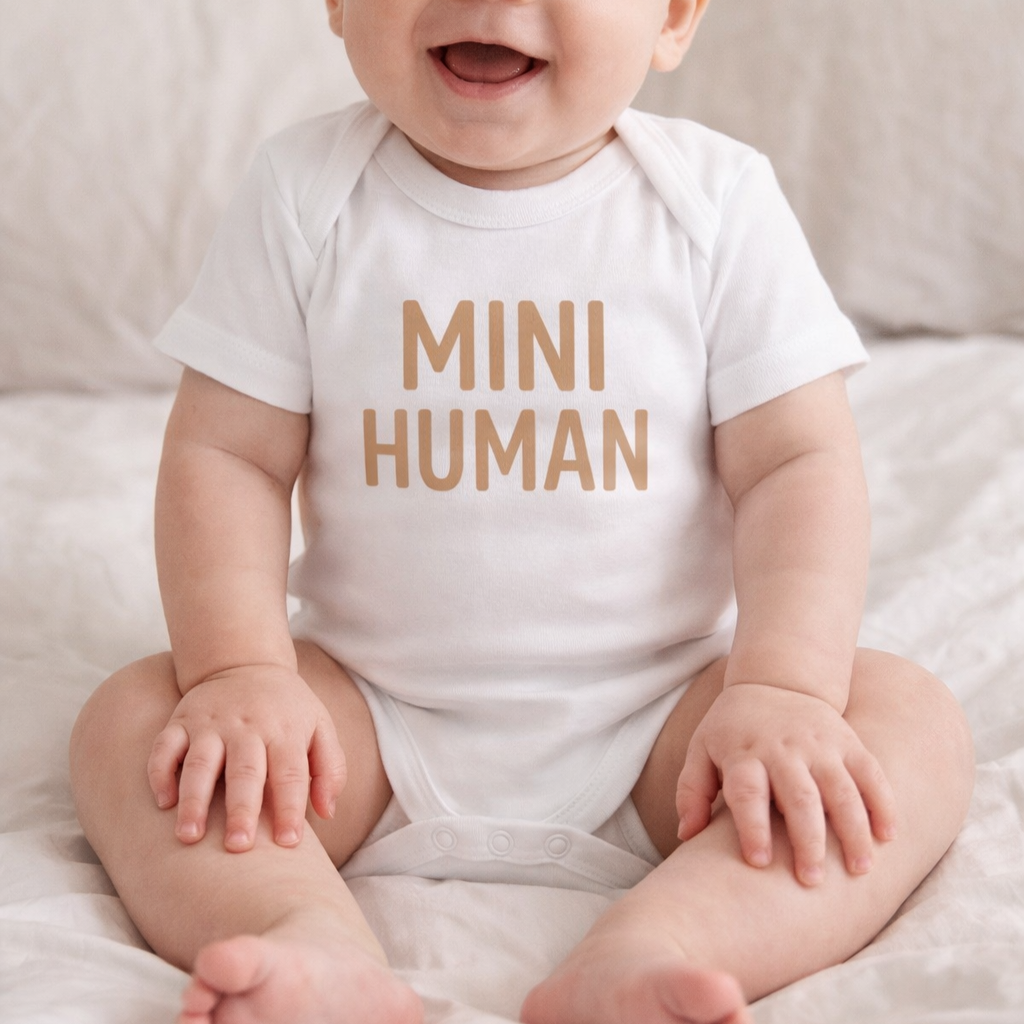 Baby wearing a white onesie with 'MINI HUMAN' text