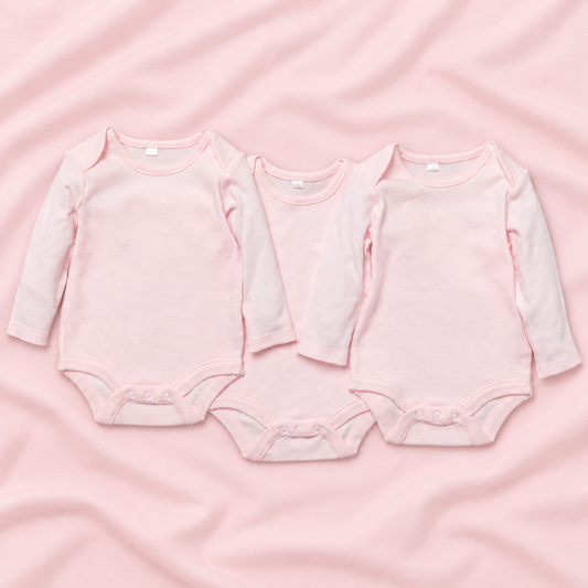 Three long-sleeve baby bodysuits in soft light pink, arranged side by side on a matching pink fabric background.