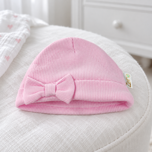 A light pink ribbed knit baby beanie with a matching fabric bow on the front. 
