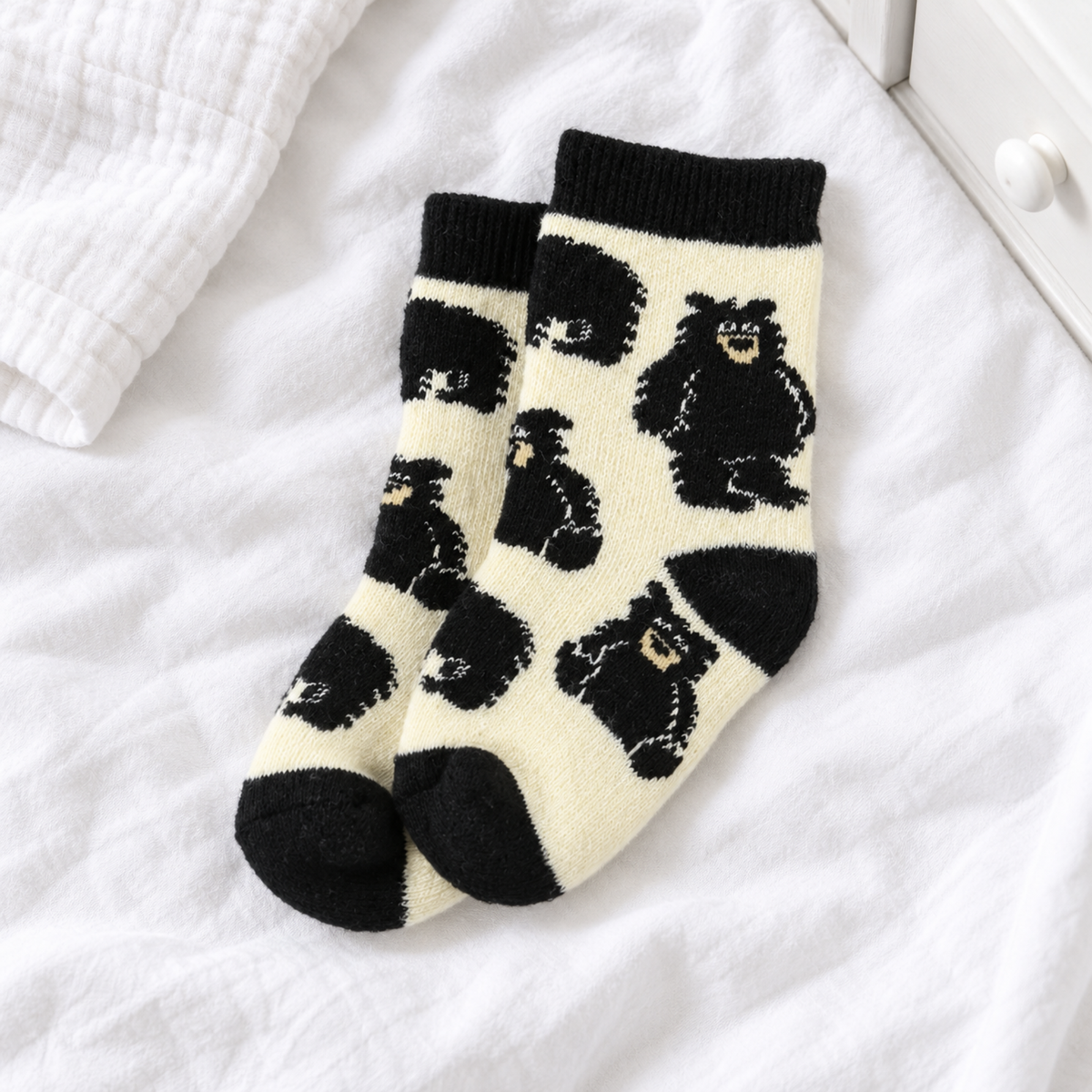 A pair of cream-colored socks with black knit cuffs, heels, and toes, featuring a playful pattern of black cartoon bears. 