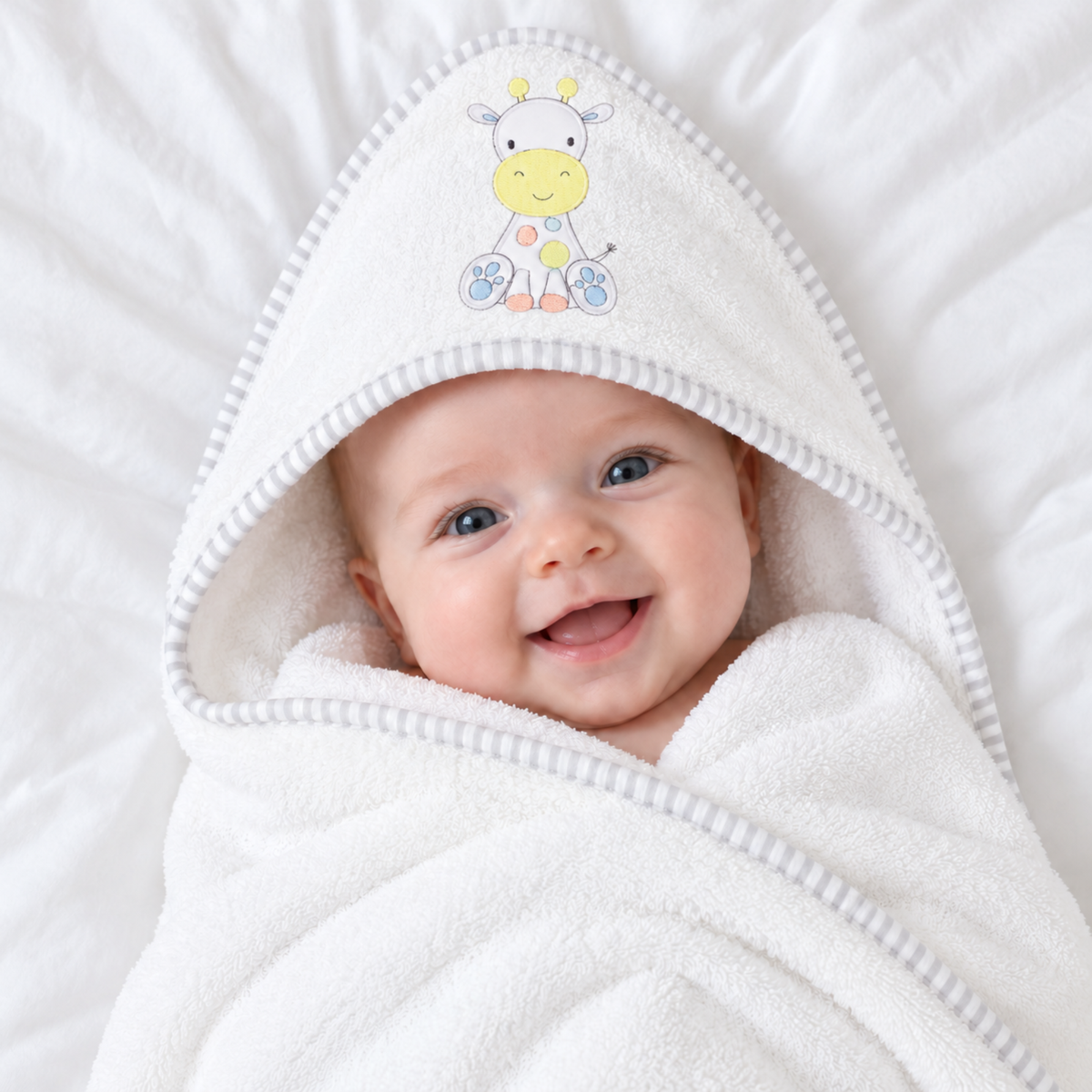White cotton hooded baby bath towel with cute pastel giraffe design and grey striped trim, wrapped around a baby.