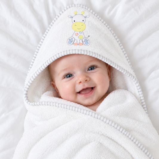 White cotton hooded baby bath towel with cute pastel giraffe design and grey striped trim, wrapped around a baby.
