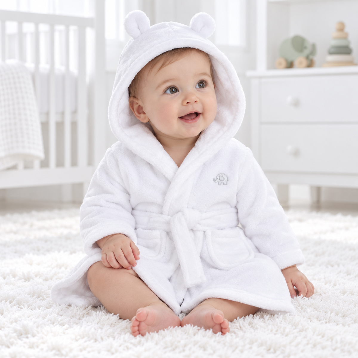 Smiling baby wearing a white plush hooded bathrobe with bear ears and elephant embroidery